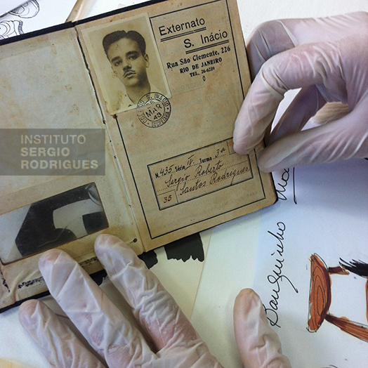 Photograph of the cleaning and conservation process done for Instituto Sergio Rodrigues' collection. The document shown is a school record of Sergio Rodrigues, at age 16, when studying at Externato Santo Inácio and dated 1943.